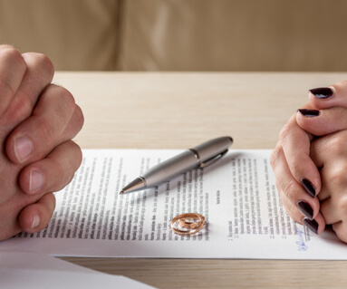 divorce document in the middle of two people and their wedding rings